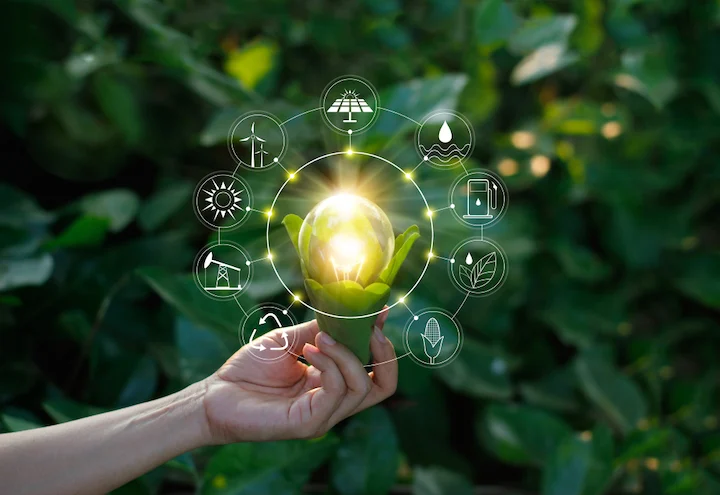 A hand holding a glowing light bulb surrounded by renewable energy icons